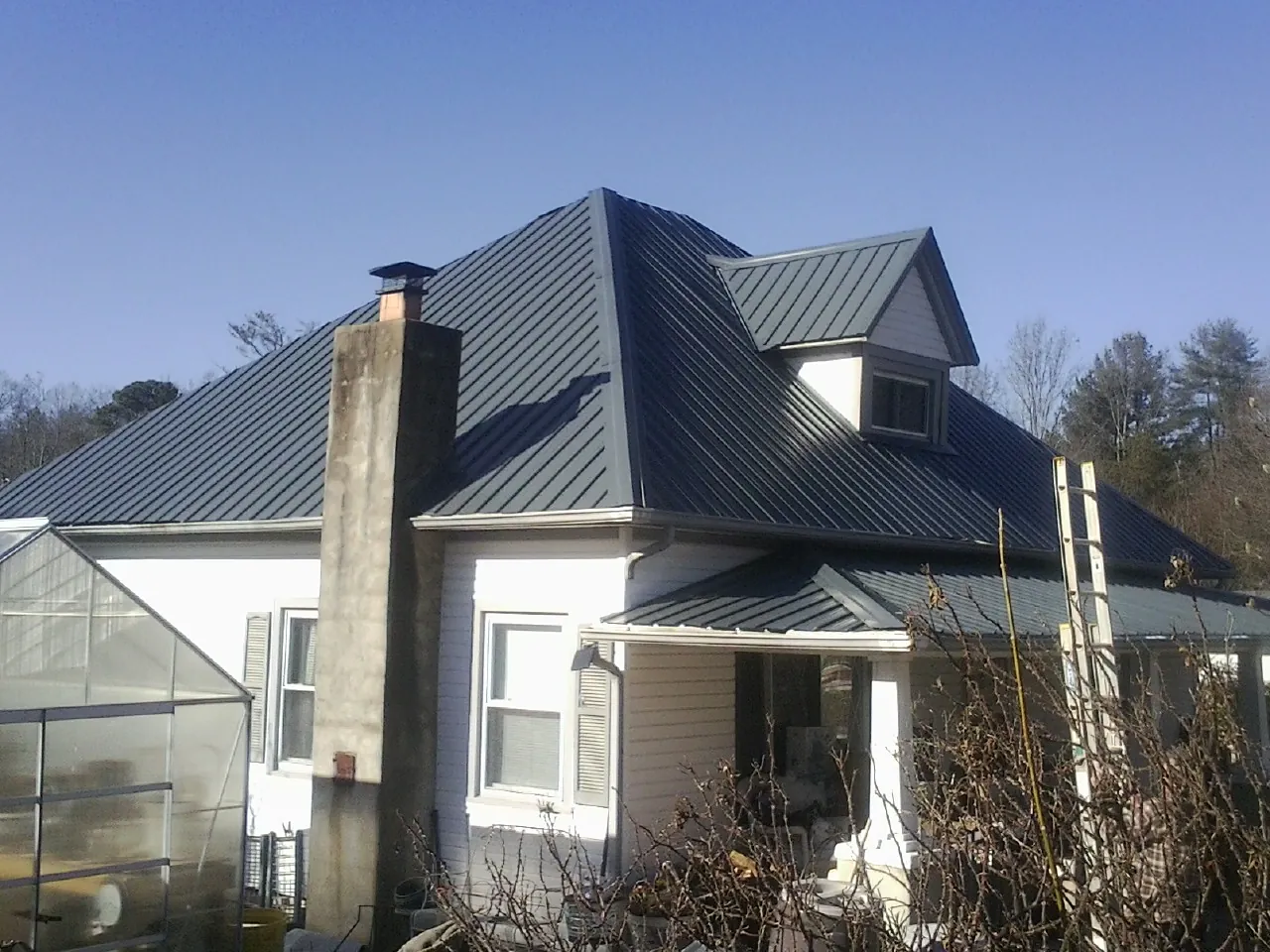 Dark blue standing seam metal roof on a white farmhouse with dormer in Trenton